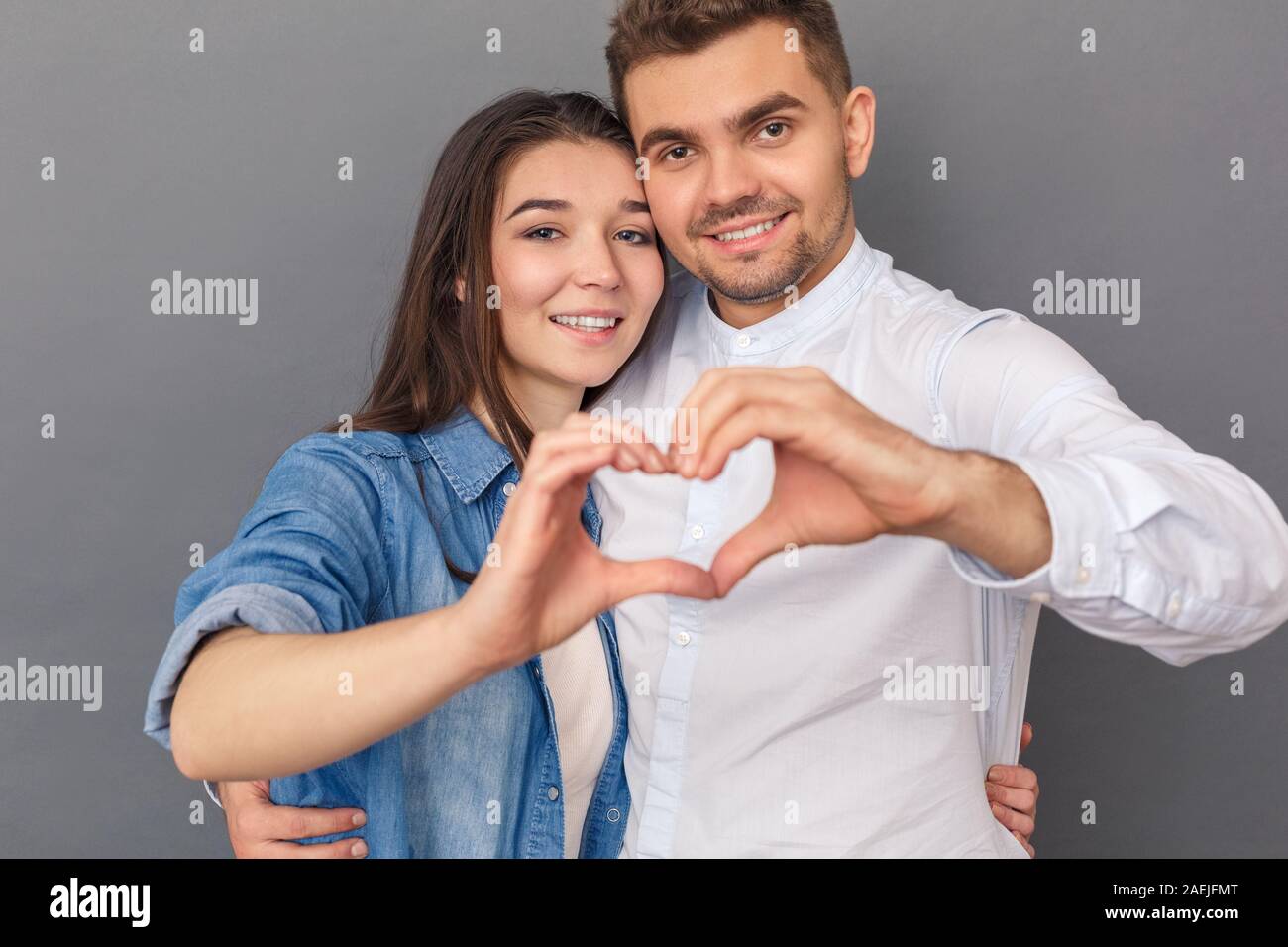 Beziehung Konzept. Junges Paar Studio stehen auf Grau umarmen, Herzform mit Händen lächelt glücklich zu Kamera schließen isoliert - oben Stockfoto