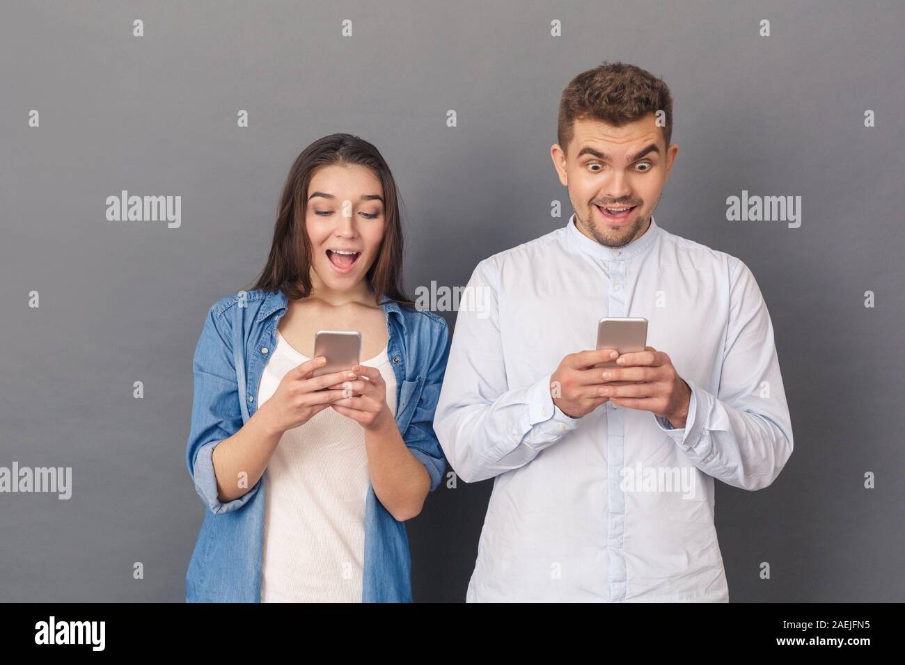 Zur Verwendung der Geräte. Junges Paar Studio stehen auf grau auf Bildschirm des Smartphones überrascht Förderung isoliert Stockfoto