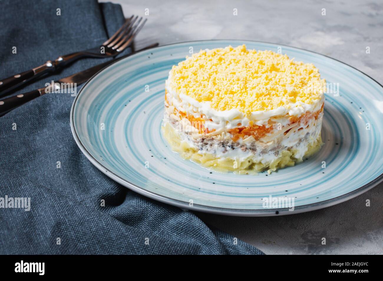 Die traditionellen russischen Salat Mimosa mit Sardinen, Zwiebeln, Kartoffeln, Karotten, Käse, Eier, Mayonnaise auf konkrete Tabelle Stockfoto