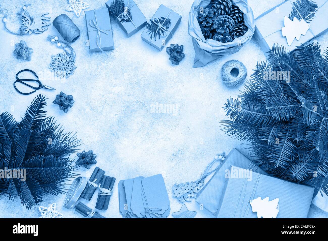 Null Abfall umweltfreundliche Weihnachten Rahmen in trendigen Classic blau Tönen. Xmas Tree Niederlassungen in Baumwolltasche, präsentiert in braunes Papier, kiefernzapfen Tags hessische Cinnamon Sticks für die Dekoration. Ansicht von oben, selektiver Fokus Stockfoto