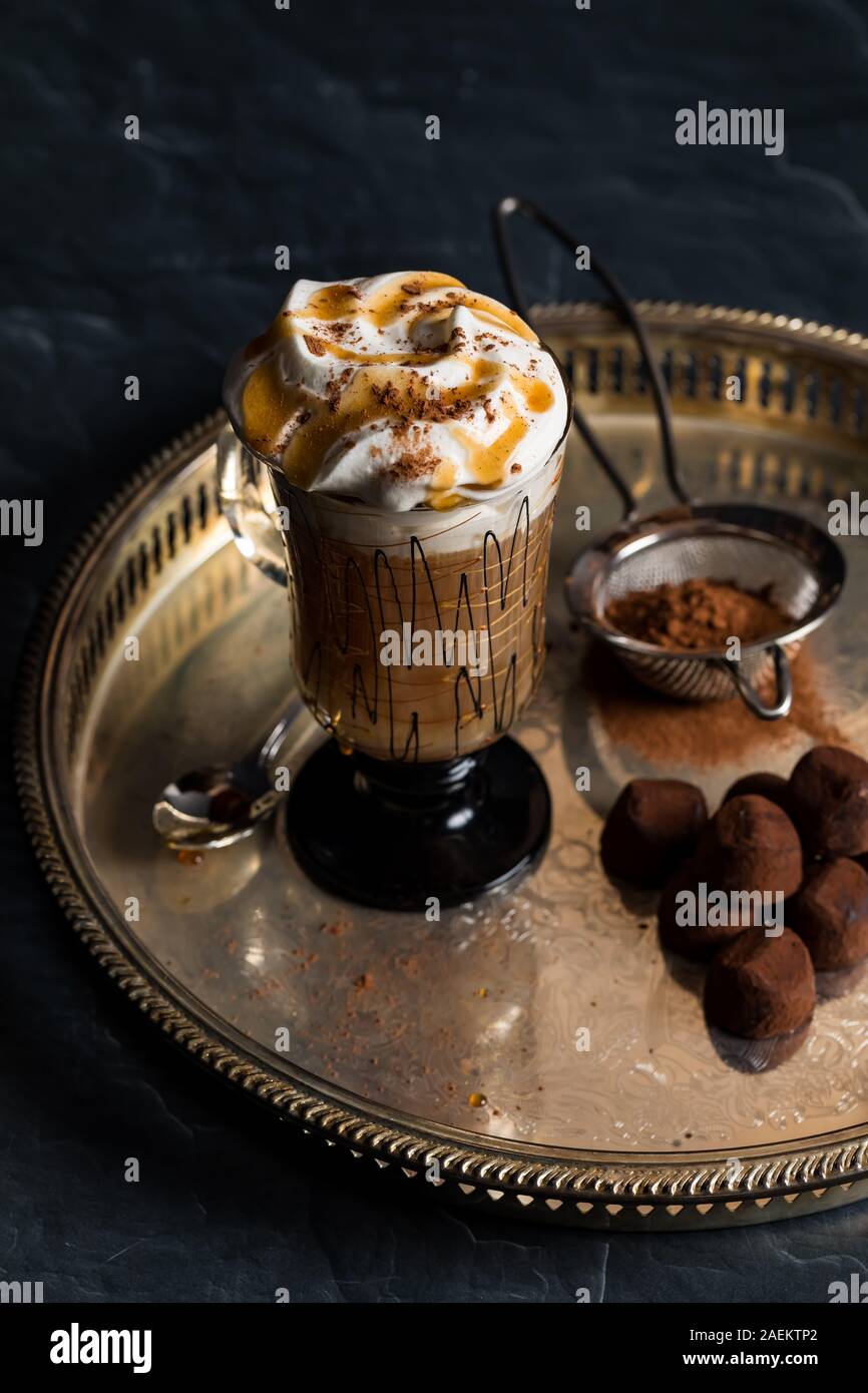 Eine Top-down-Sicht auf ein dekoratives Glas heißen Cappuccino und Sahne und garniert mit Kakao bestreut und serviert mit Trüffeln. Stockfoto