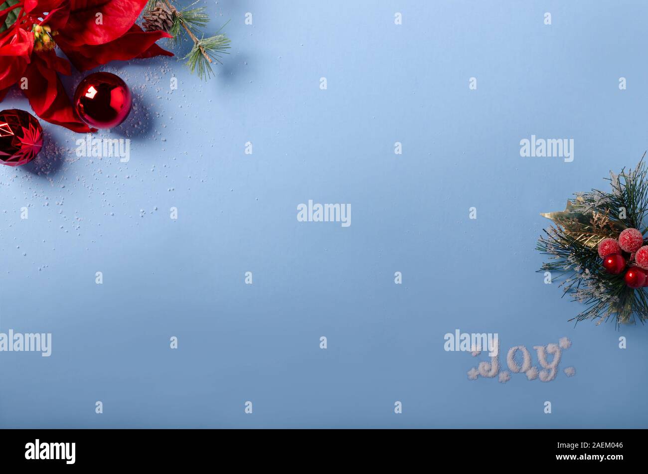 Studio-Weihnachts-Flat-Lay mit roter Verzierung, Poinsettia, Grünzeug, Joyful-Schnee-Effekt-Schriftzug und Kopierraum auf blauem Hintergrund. Stockfoto