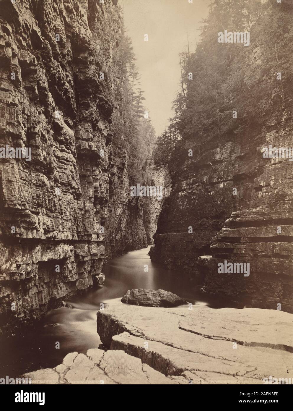 Dieses Landschaftsfoto von Seneca Ray Stoddard, um 1880, zeigt Ausable Chasm aus dem Fluss nahe Table Rock. Sie zeigt felsige Klippen, Flussläufe, bewaldete Ufer und natürliche Landschaften, die typisch für die amerikanische Landschaftsfotografie des 19. Jahrhunderts sind. Stockfoto