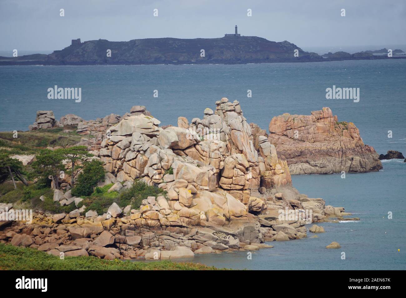 Sonne auf der rosa Granit Küste der Bretagne, Frankreich mit einer kleinen Insel und Leuchtturm am Horizont Stockfoto