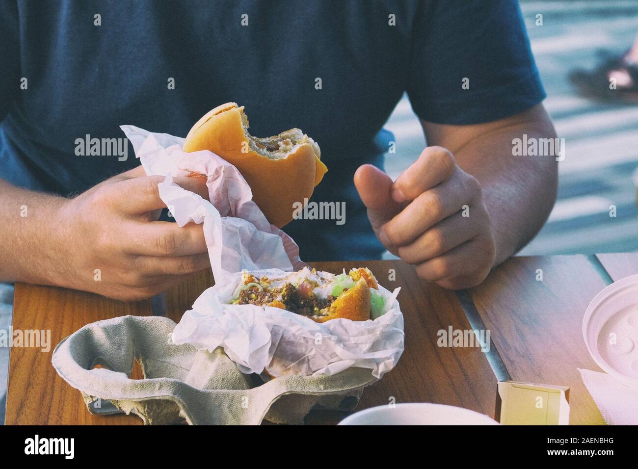 American cheese Burger in der Hand in ein Cafe. Essen in einem Restaurant und geniessen die hervorragende fast food. Getönten Bild. Stockfoto