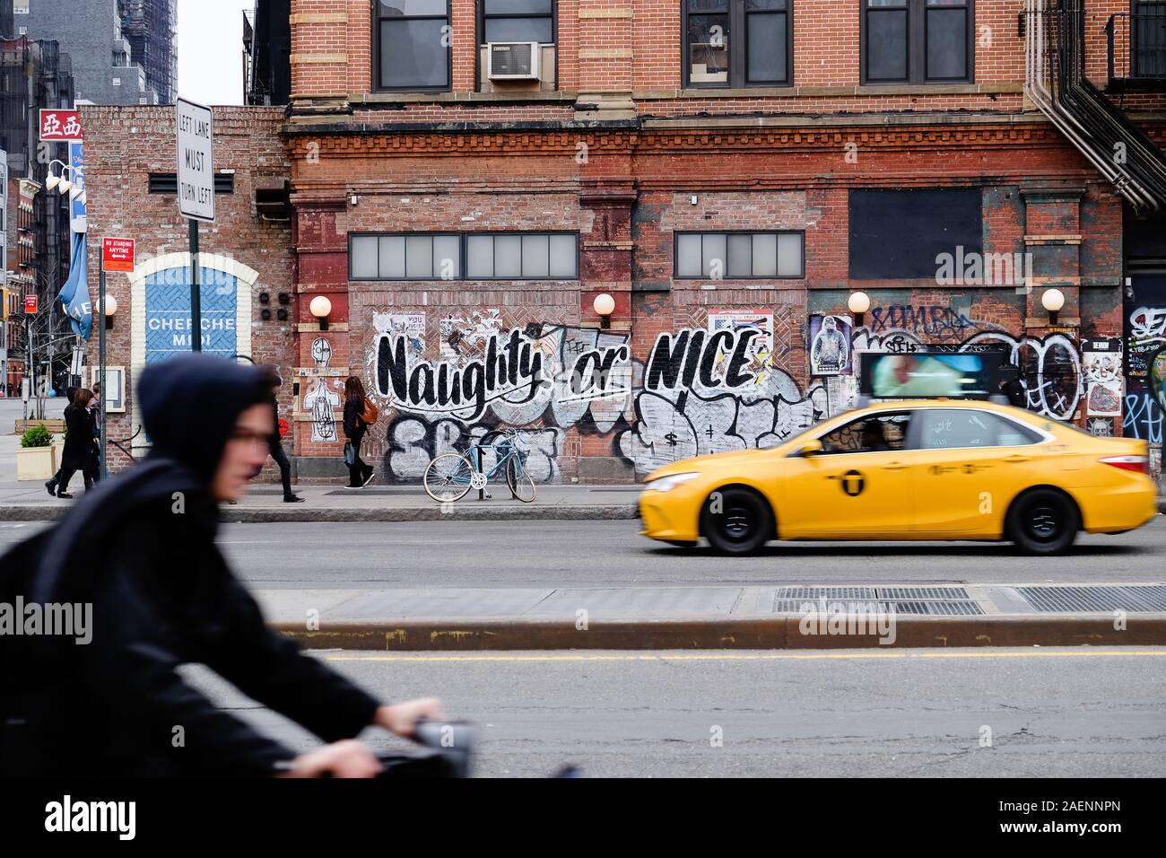 Böse oder Nett graffiti auf New York Street mit unscharfen Radfahrer und Taxi Stockfoto