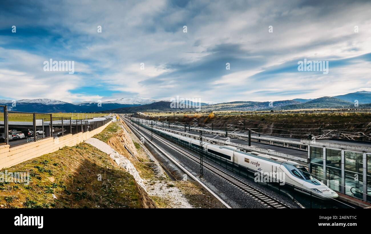 Segovia, Spanien - Dez 9, 2019: Ave-Renfe Zug zieht in Segovia Bahnhof mit schneebedeckten Bergen im Hintergrund Stockfoto