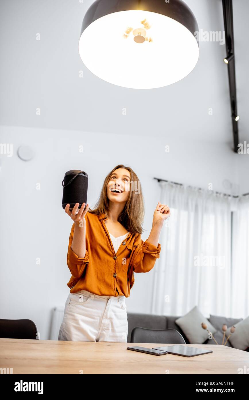 Glückliche Frau controlling home Licht mit einem smart Lautsprecher im Wohnzimmer. Konzept einer Smart Home und Lichtsteuerung mit Sprachbefehlen Stockfoto