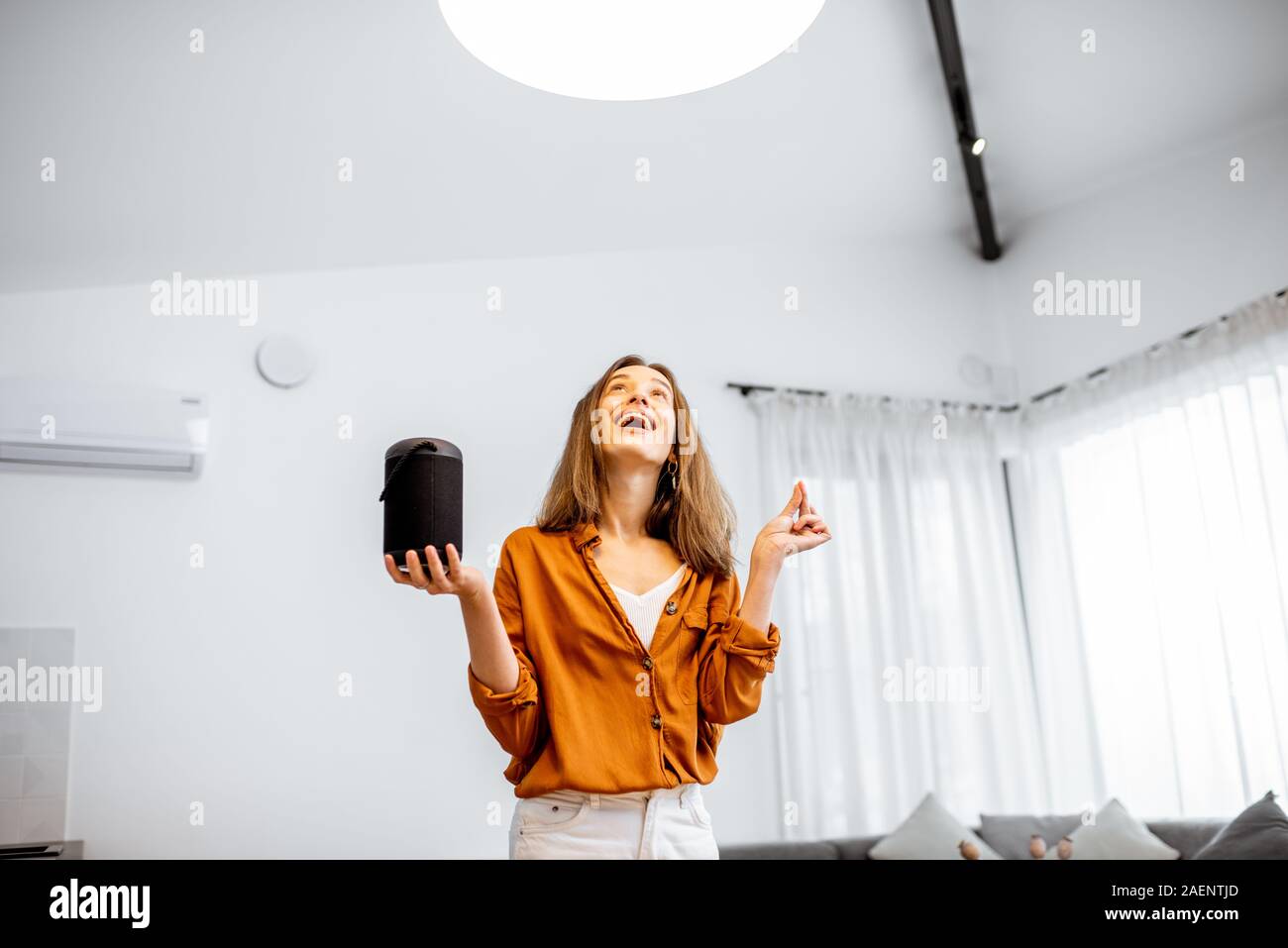 Glückliche Frau controlling home Licht mit einem smart Lautsprecher im Wohnzimmer. Konzept einer Smart Home und Lichtsteuerung mit Sprachbefehlen Stockfoto