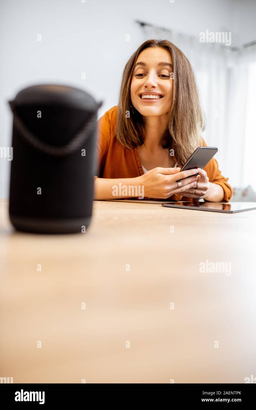 Junge fröhliche Frau controlling home Geräte mit einem Sprachbefehle, um eine Smart Spalte zu Hause sprechen. Konzept der "Smart Home" und Sprachsteuerung Stockfoto