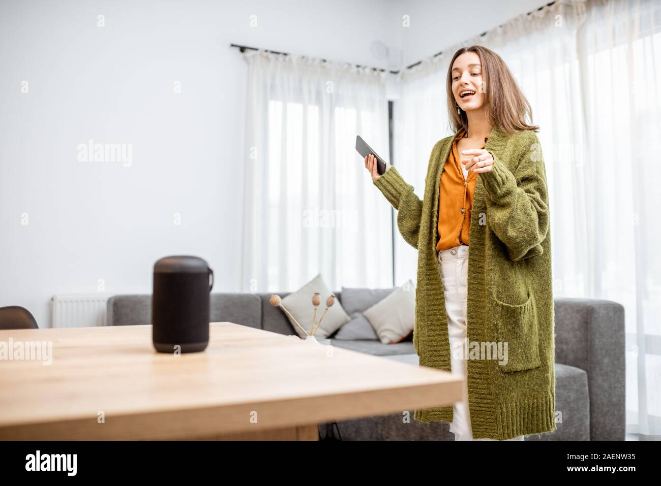 Junge fröhliche Frau controlling home Geräte mit einem Sprachbefehle, um eine Smart Spalte zu Hause sprechen. Konzept der "Smart Home" und Sprachsteuerung Stockfoto