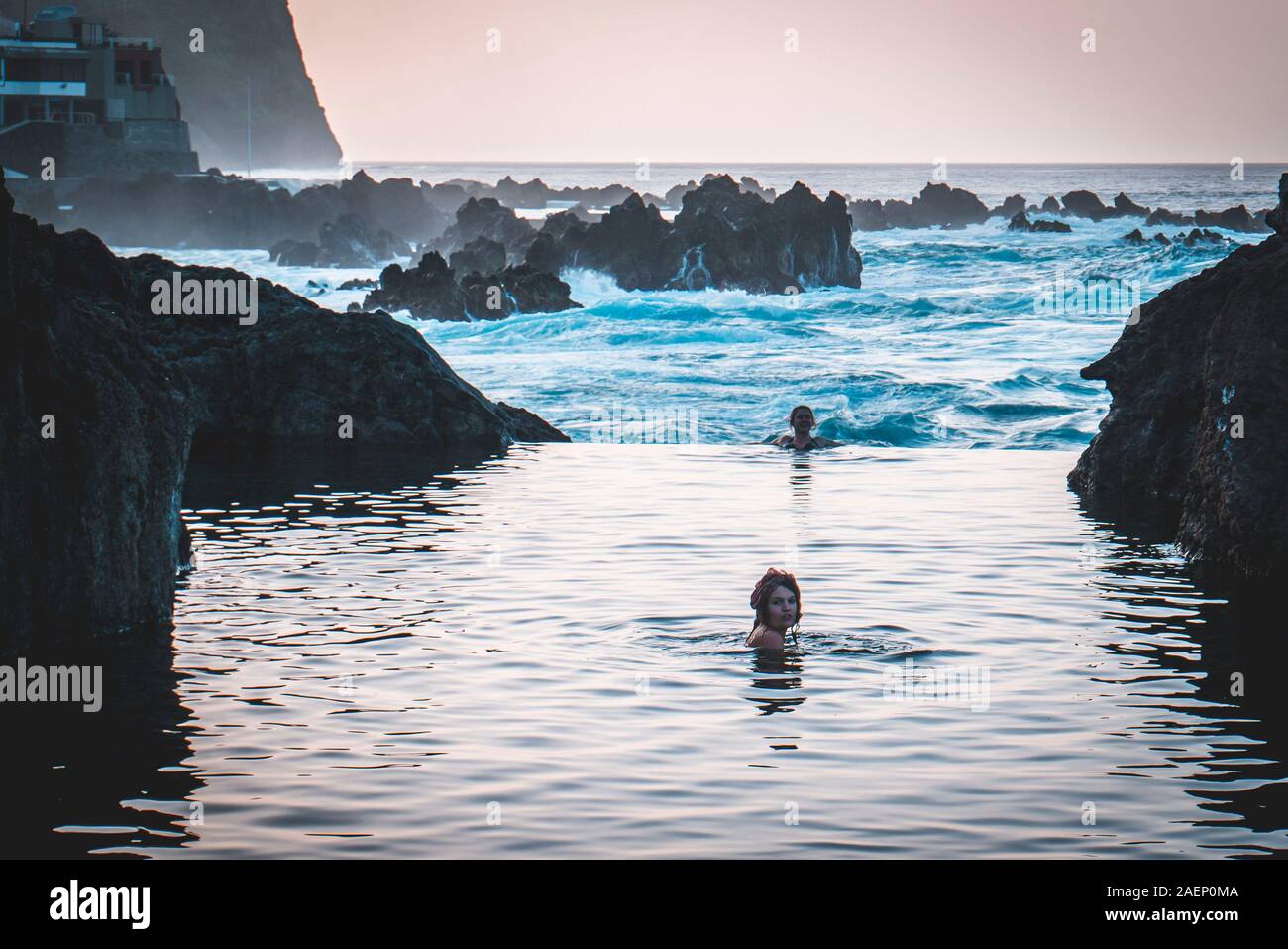 Portugal, Madeira: junge frau Schwimmen in einem natürlichen Meerwasserschwimmbecken von Felsen umgeben, in Porto Moniz, mit dem Meer im Hintergrund Stockfoto