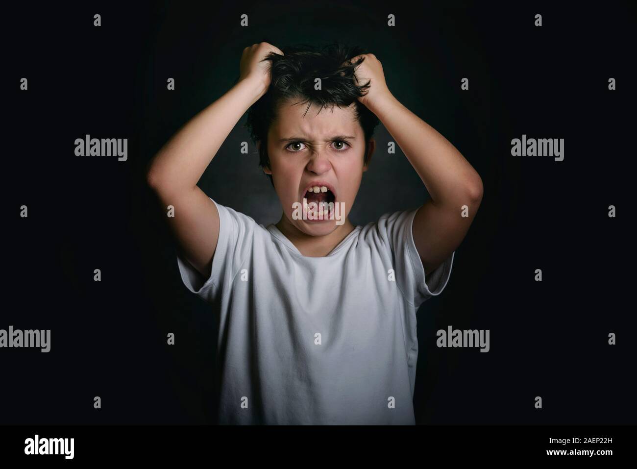 Wütend Junge, der seine Haare auf schwarzem Hintergrund zieht Stockfoto