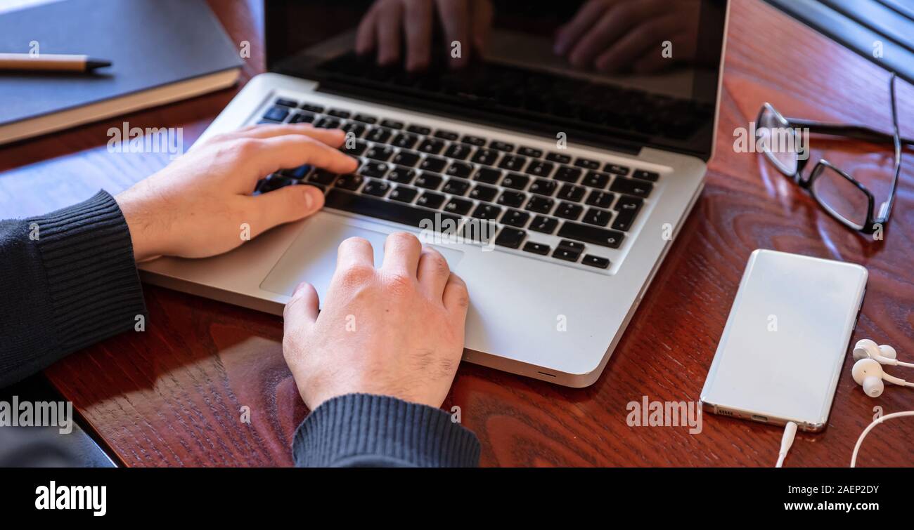 Mann bei der Arbeit mit einem Computer Laptop auf Holz Büro Schreibtisch, hohen Winkel Detailansicht Stockfoto