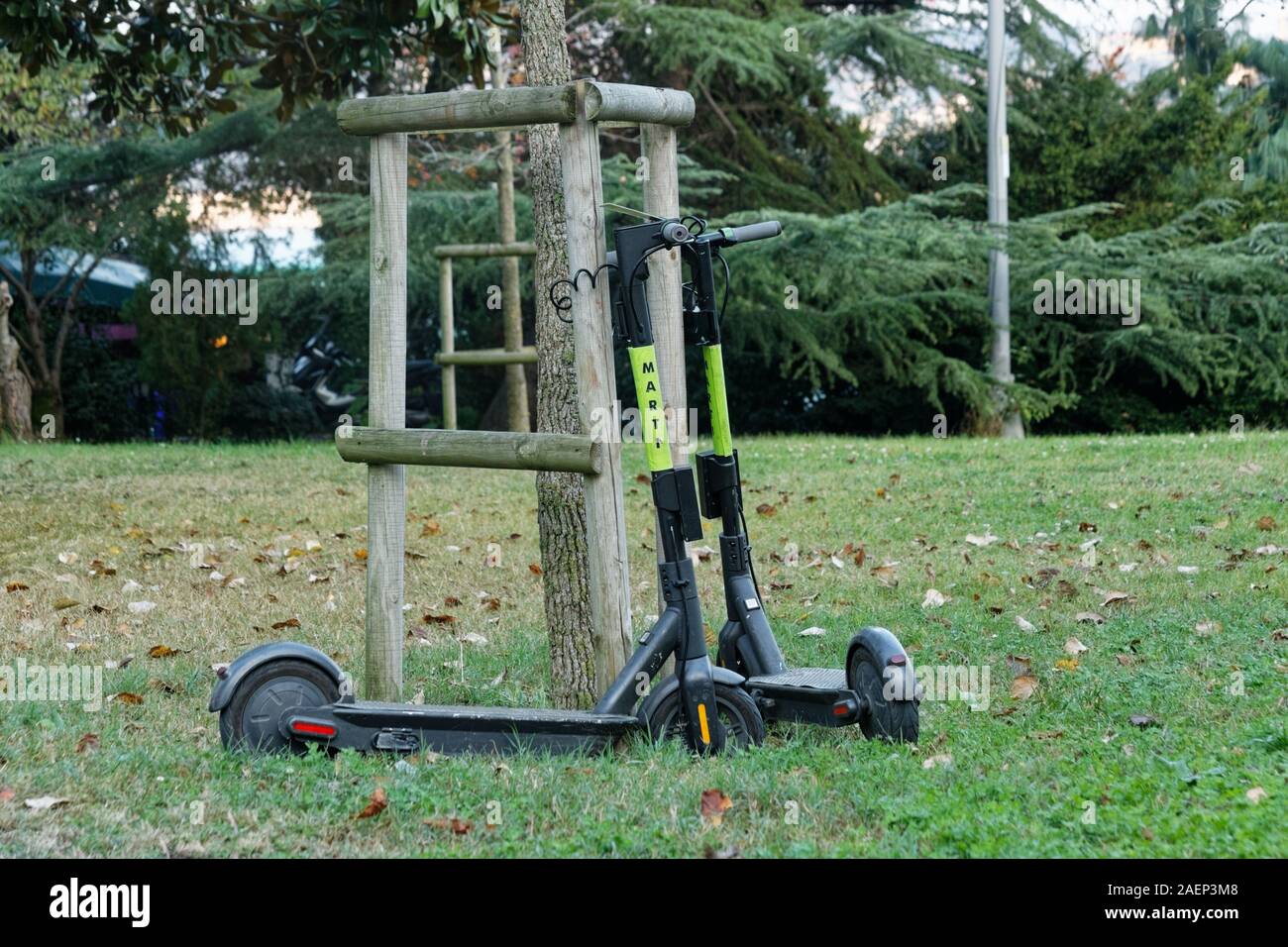 Zwei Elektroroller von Marti Tech, Motorrollerverleih, an einen Baum und wartet gemietet werden. Bäume, Gras und Blätter im Herbst auf der Rückseite. Stockfoto