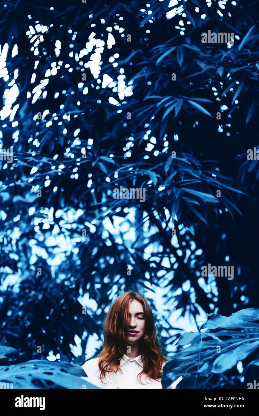 Schöne junge rothaarige Frau in tropischen Garten Farben in Blau. Stockfoto