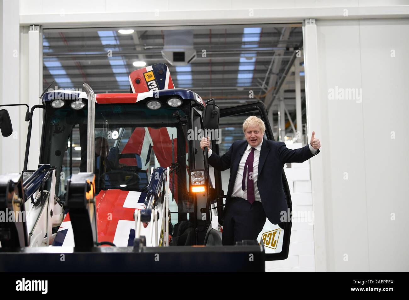 Premierminister Boris Johnson Gesten nach dem Fahren einer Union Flag-themed JCB, mit den Worten 'Brexit getan" innerhalb der Bagger Schaufel, durch eine gefälschte Wand prangt das Wort "verkehrsinfarkt", bei einem Besuch in JCB Cab Manufacturing Center in Uttoxeter, während auf der allgemeinen Wahlkampagne Trail. Stockfoto