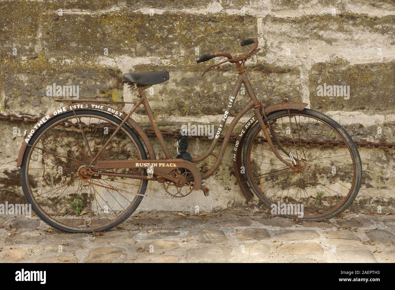 Ein altes rostiges Fahrrad angekettet an eine Wand in Paris. Rost im  Frieden geschrieben auf der Seite haben Stockfotografie - Alamy