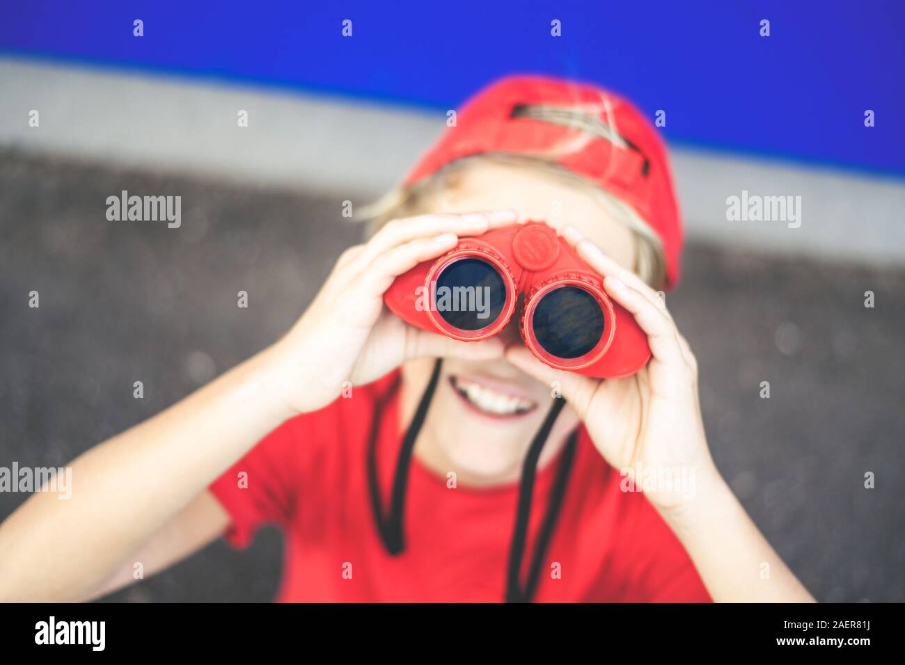 Schöne junge weg schauen mit einem roten Fernglas auf einem blauen Hintergrund. Bunte Bild einer jungen männlichen Spaß mit einem Teleskop. Spaß Stockfoto