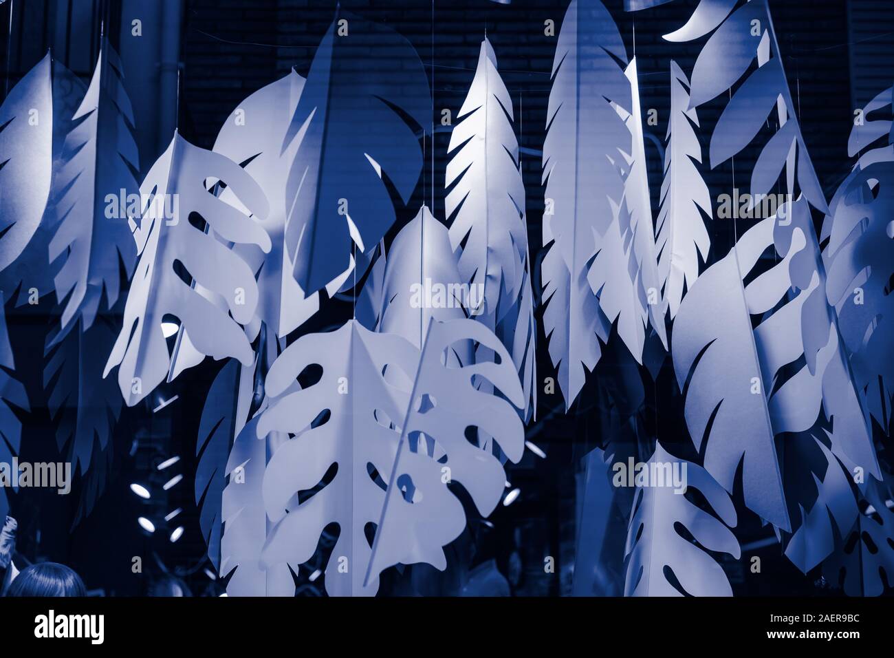 Hängende große Hand Papier tropische Blätter getönten in trendigen blau gemacht. Kreative Schaufenster Dekoration. Modernes, minimalistisches Hintergrund. Farbe des Ja Stockfoto