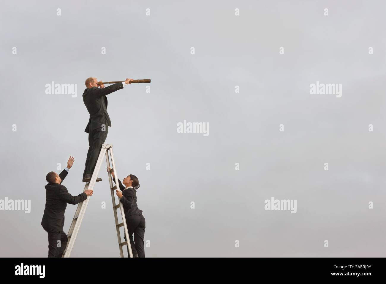 Ein Geschäftsmann stehen auf der obersten Sprosse einer hohen trittleiter schaut durch ein Teleskop als männliche und weibliche Kollegin Aufstieg auf der Leiter. Stockfoto