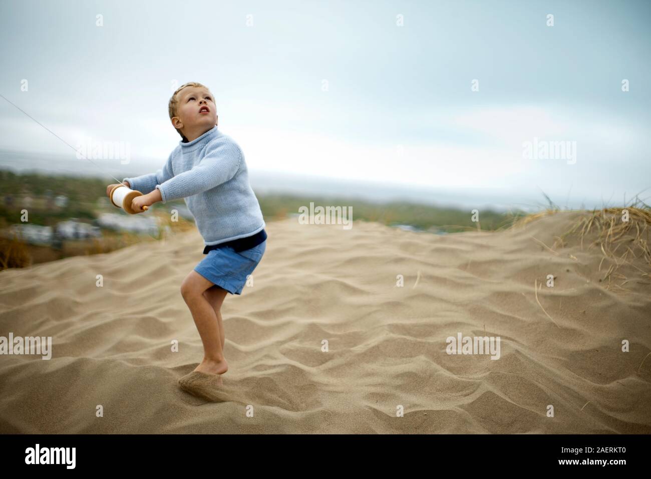 Junge sieht aus, als er ein 1-string kite Holz Haspel steuert beim Stehen auf einer Sanddüne. Stockfoto