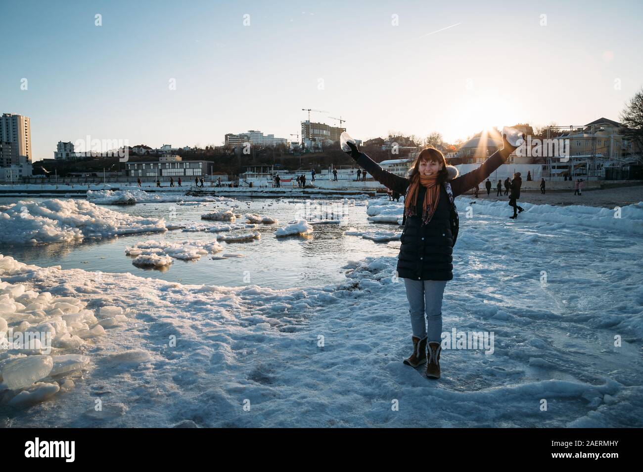 Odessa, Ukraine - Februar, 16 2017: junge lächelnde Frau, die auf gefrorenen Küste des Schwarzen Meeres mit Eis holding Stück Eis bei Sonnenuntergang fällt. Stockfoto