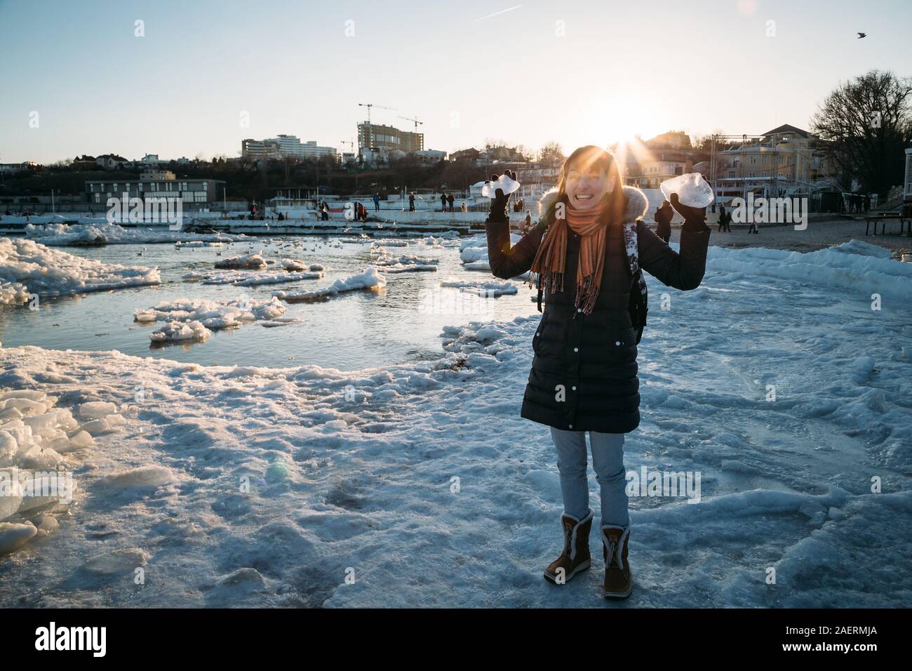 Odessa, Ukraine - Februar, 16 2017: junge lächelnde Frau, die auf gefrorenen Küste des Schwarzen Meeres mit Eis holding Stück Eis bei Sonnenuntergang fällt. Stockfoto