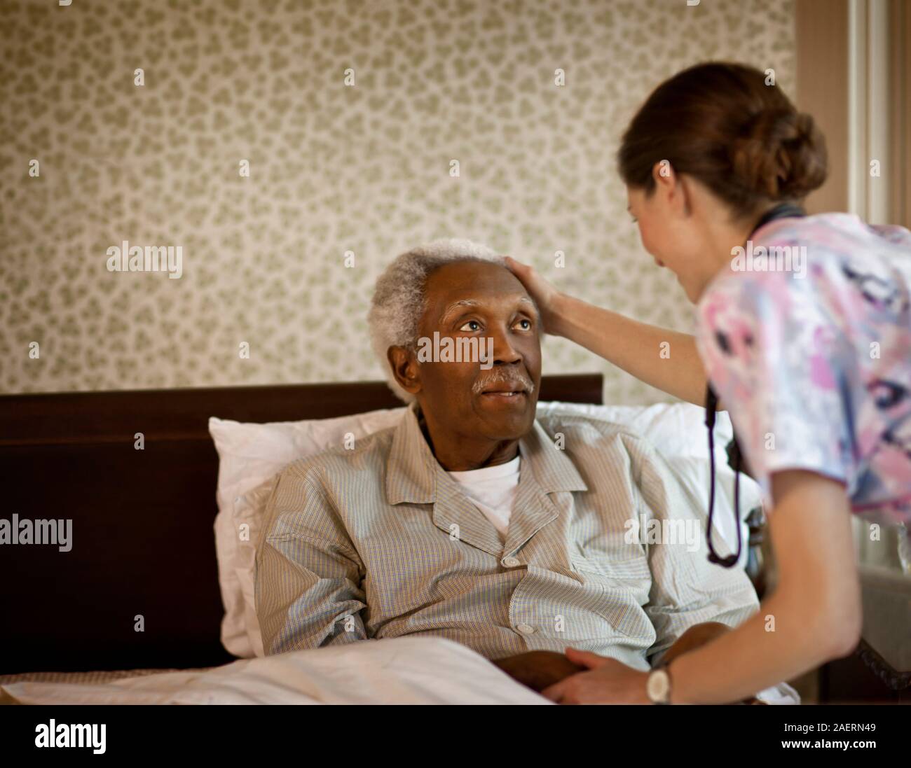 Junge Krankenschwester hält die Hand und berührt den Kopf ihres älteren männlichen Patienten. Stockfoto