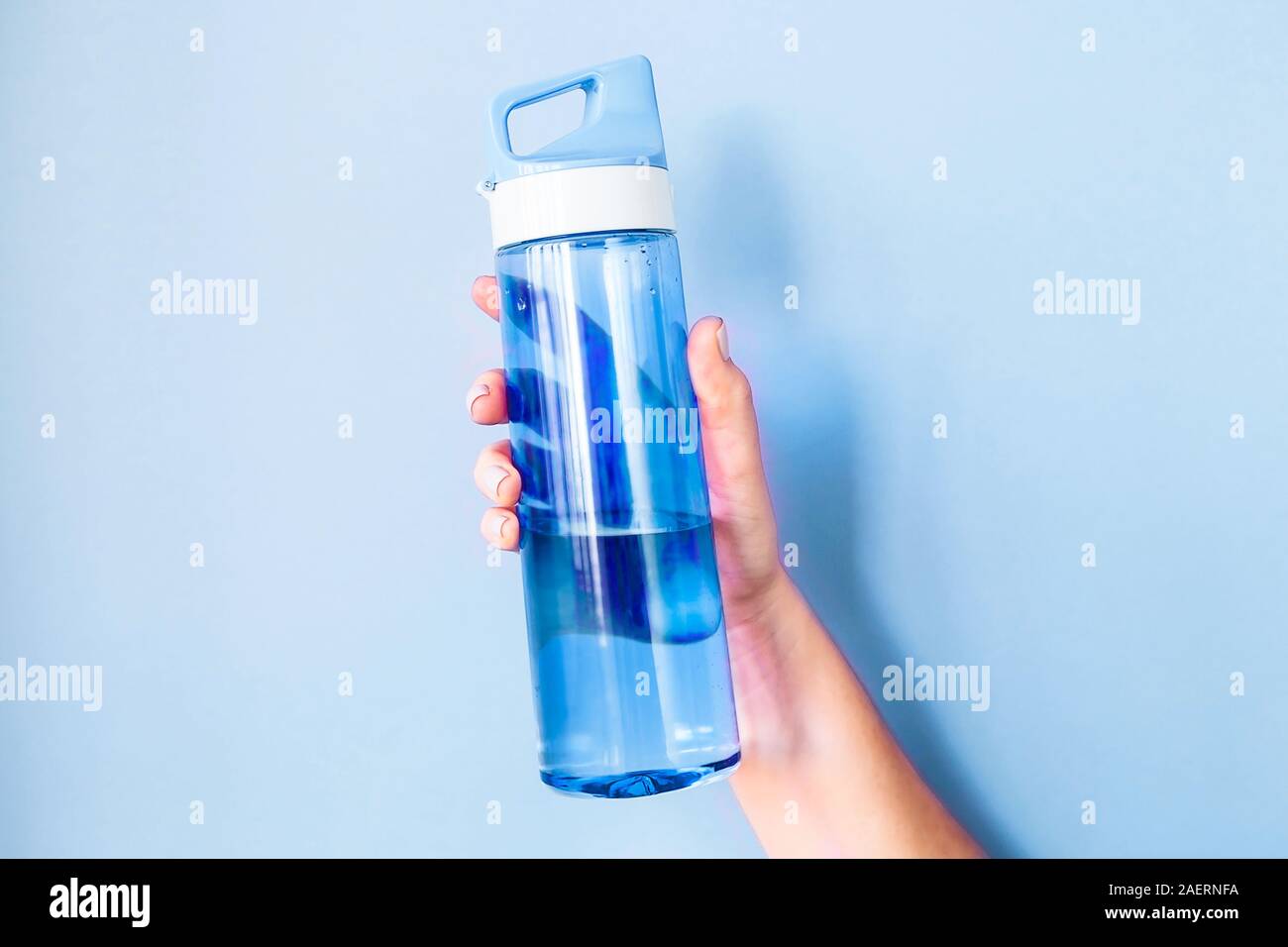 Hält eine Frau blaue Flasche Wasser in der Hand, für den Sport. Auf einem hellen Hintergrund. Gesunder Lebensstil und Fitness Concept im klassischen 2020 Farbe des Ja Stockfoto