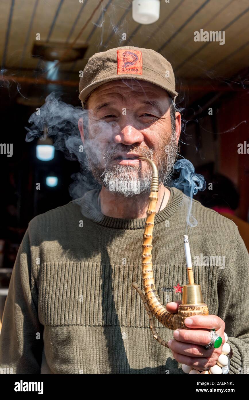 März 14, 2019: Ältere Bai ethnische Minderheit Mann Rauchen einer Pfeife in Xizhou Dorf, Yunnan, China Stockfoto