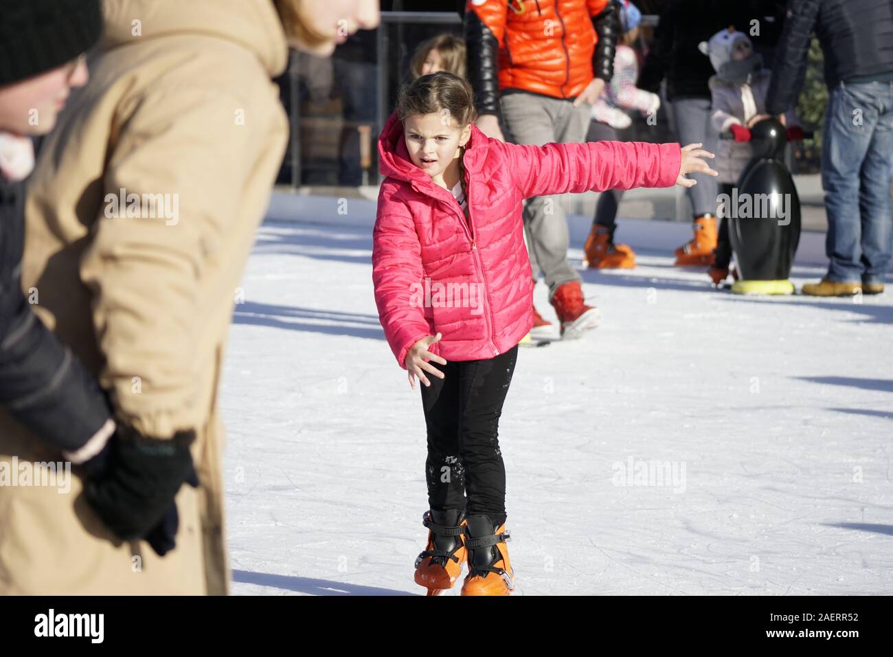 Junge Mädchen in der roten Jacke Schlittschuhlaufen auf der Eisbahn in Meran, im Dezember 2019 Stockfoto