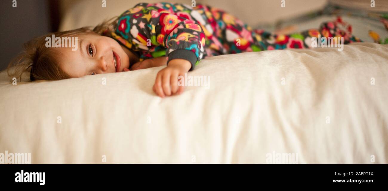 Lächelnd Kleinkind Mädchen liegt auf dem Bett im Schlafanzug. Stockfoto