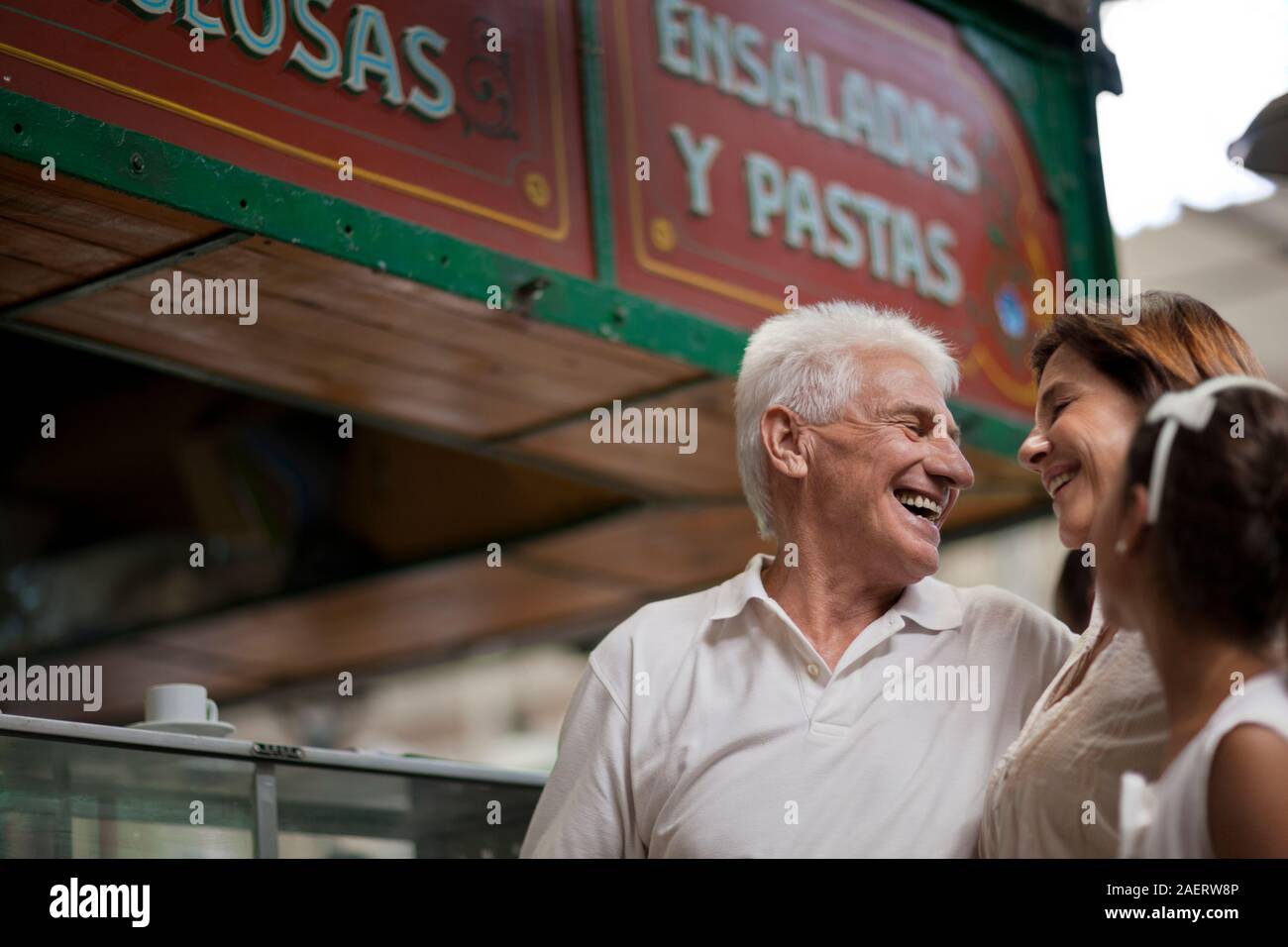 Älterer Mann und seine Frau sehen sich gegenseitig liebevoll während ihre Enkelin an schaut. Stockfoto