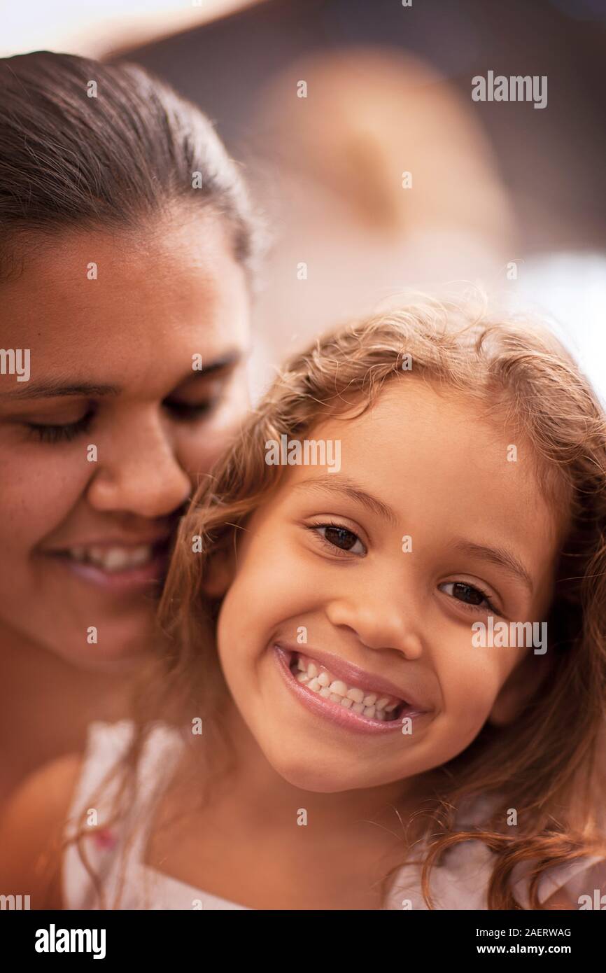 Junges Mädchen lächelt, während sie von ihrer Mutter gehalten wird. Stockfoto