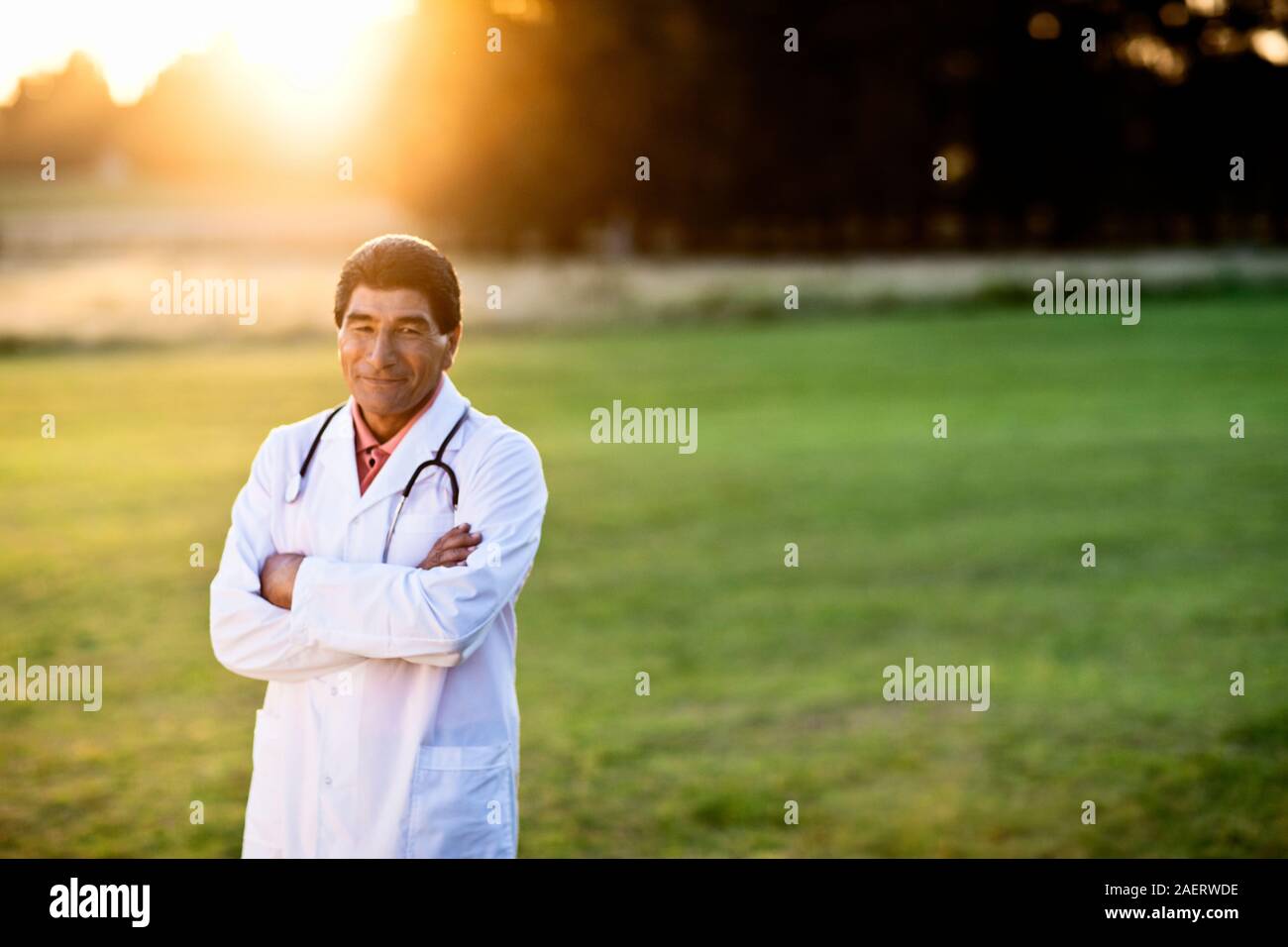Männlicher Arzt mit gekreuzten Armen Posen für ein Portrait beim Stehen in einem Feld bei Sonnenaufgang. Stockfoto