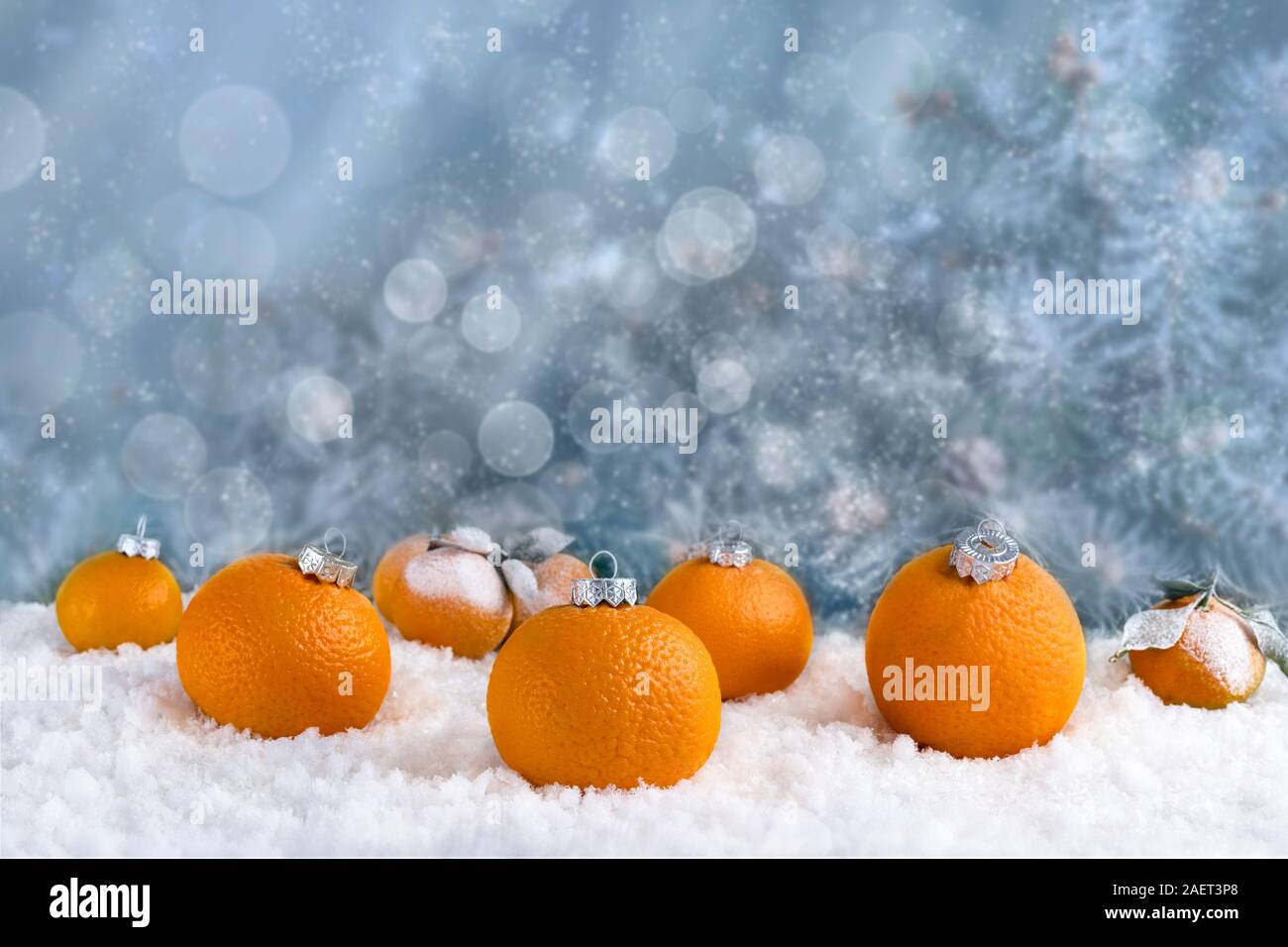 Dekorative Komposition von Christbaumschmuck aus Mandarinen auf weißem Schnee. Abstrakt Blau Hintergrund mit Lichtern und Schnee Stockfoto