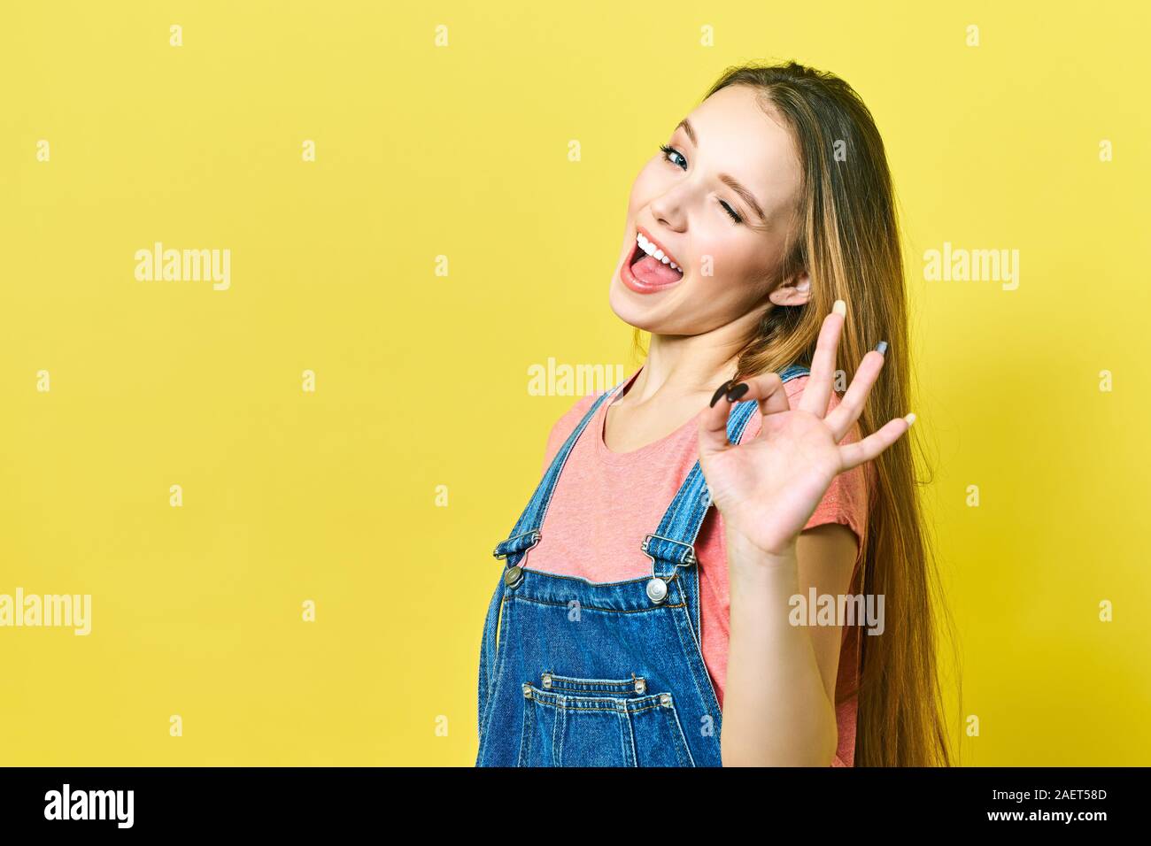 Lustige und fröhliche Mädchen zeigt okay unterzeichnen und zwinkert Kamera auf gelbem Hintergrund. Stockfoto