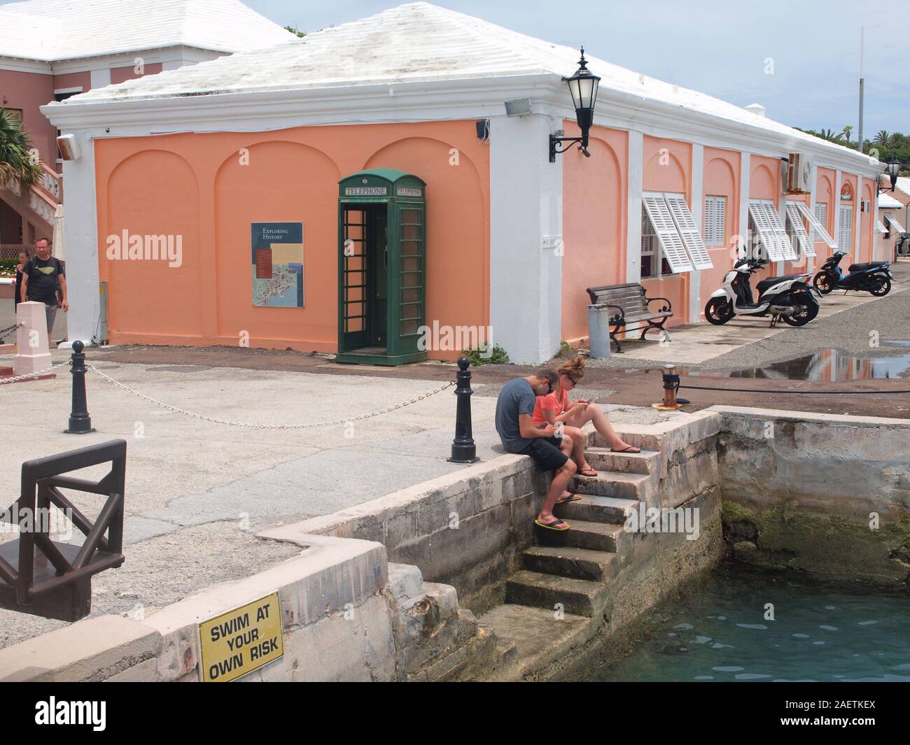 Junges Paar in sein Handy vertieft, als sie sitzen in der Nähe von St. George's Hafen in Bermuda nicht auf die Schönheit der Welt um Sie herum. Stockfoto