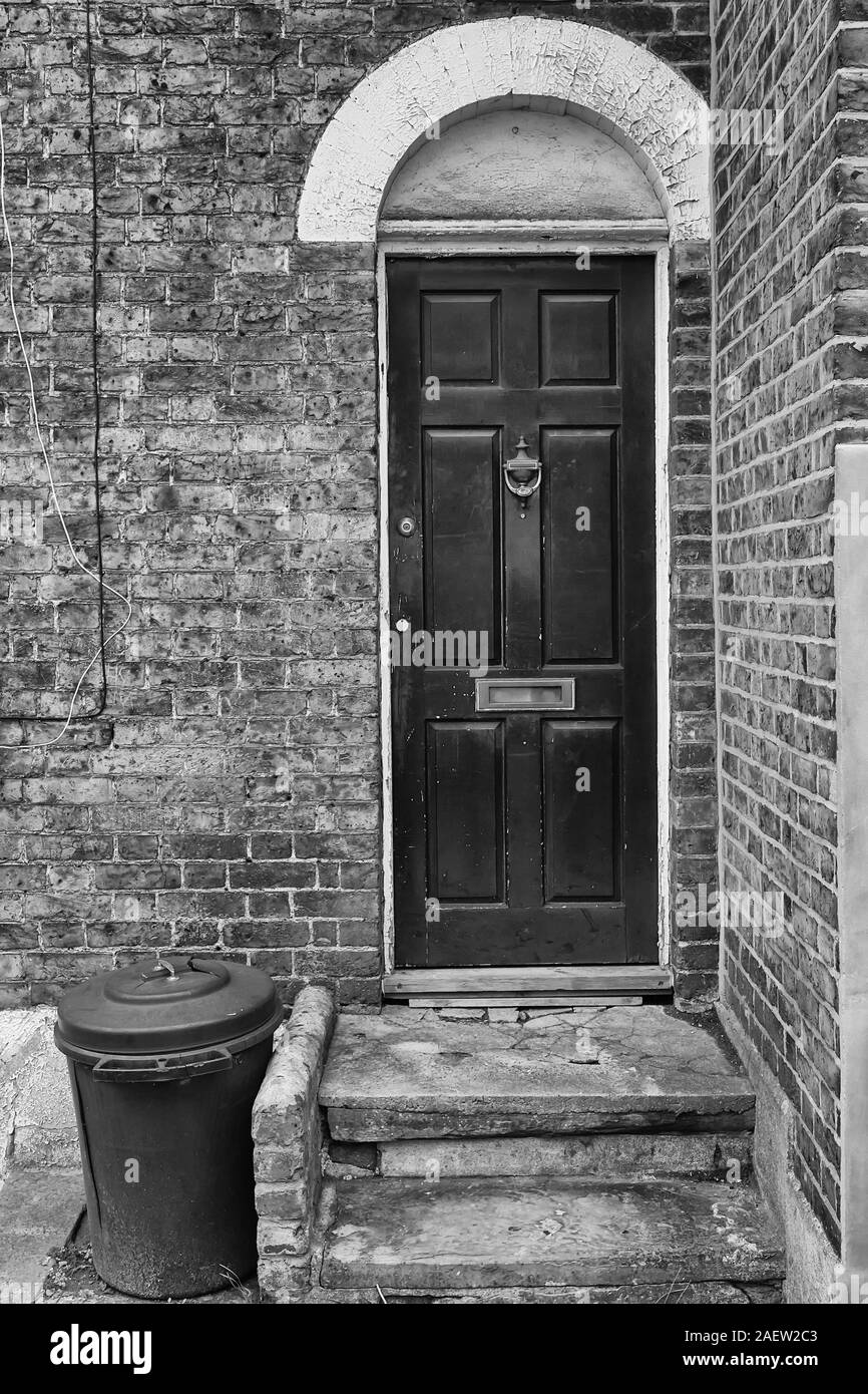 Ein Kunststoff Papierkorb steht eine alte Tür in London, England. Die Mauer hat schon bessere Tage gesehen. Stockfoto