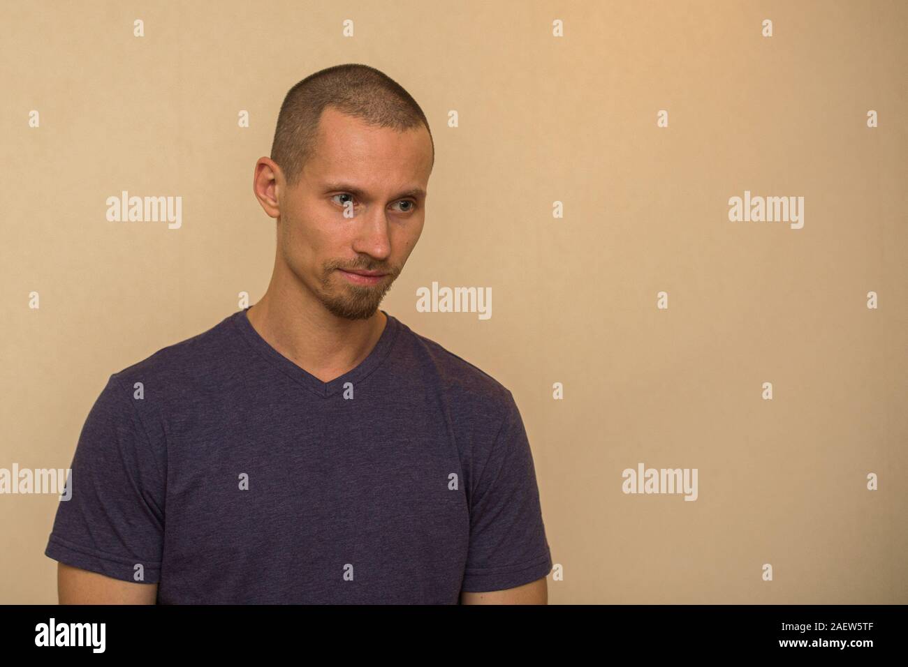 Ein attraktiver junger Mann im blauen T-Shirt stellt gegen eine beige Wand Stockfoto