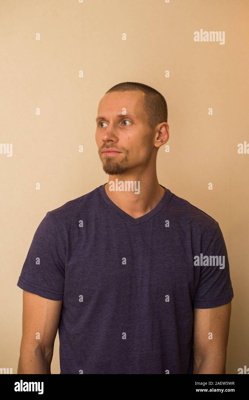 Ein attraktiver junger Mann im blauen T-Shirt stellt gegen eine beige Wand Stockfoto