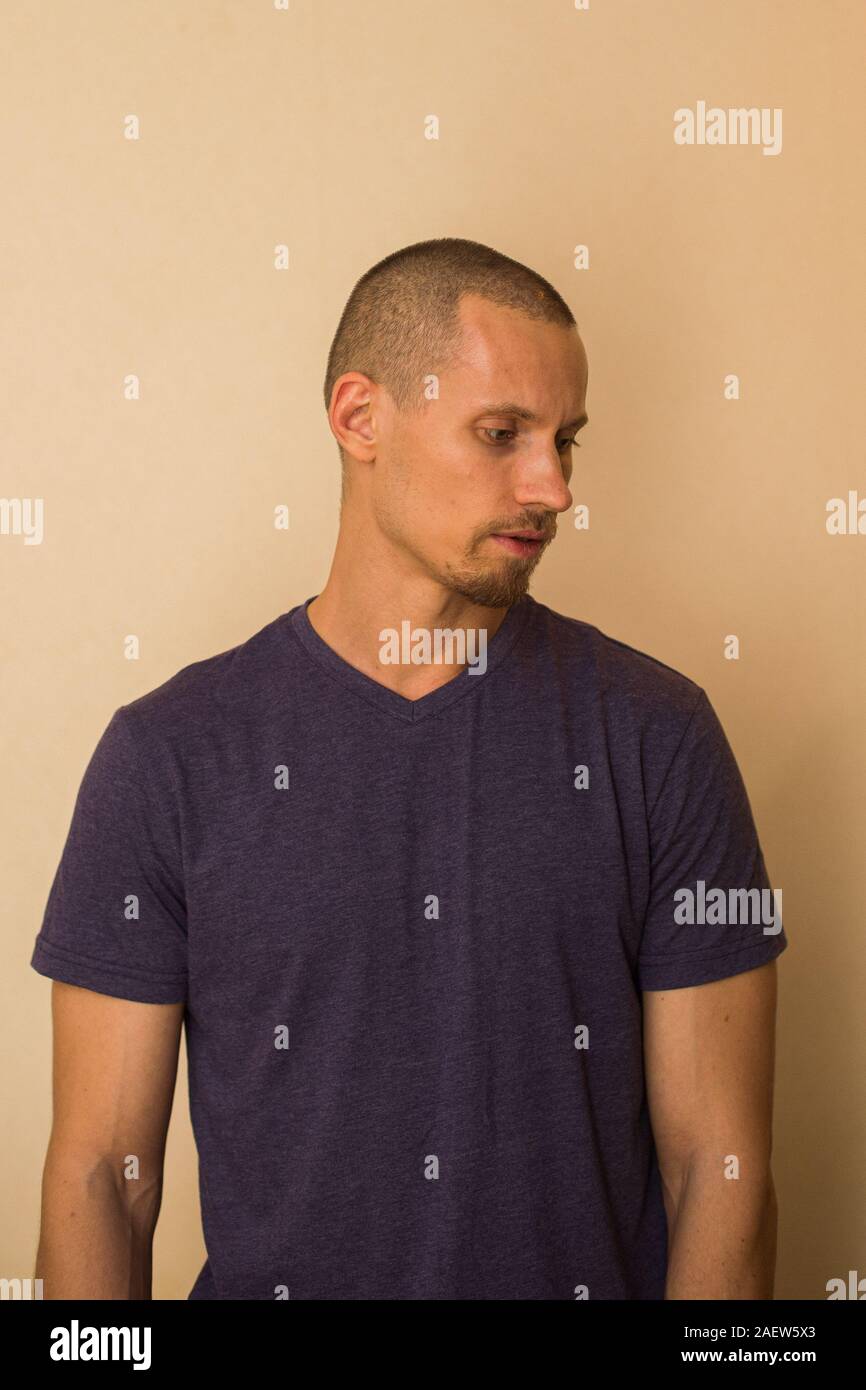 Ein attraktiver junger Mann im blauen T-Shirt stellt gegen eine beige Wand Stockfoto