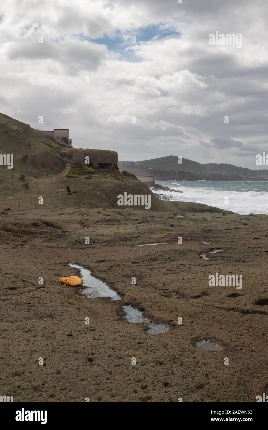 An der felsigen Küste des Mittelmeers mit verlassenen Tierheim aus dem Zweiten Weltkrieg die Zweite und. Intensive regnerischen Wolken am Frühlingshimmel. Bosa Marina, Sardin Stockfoto