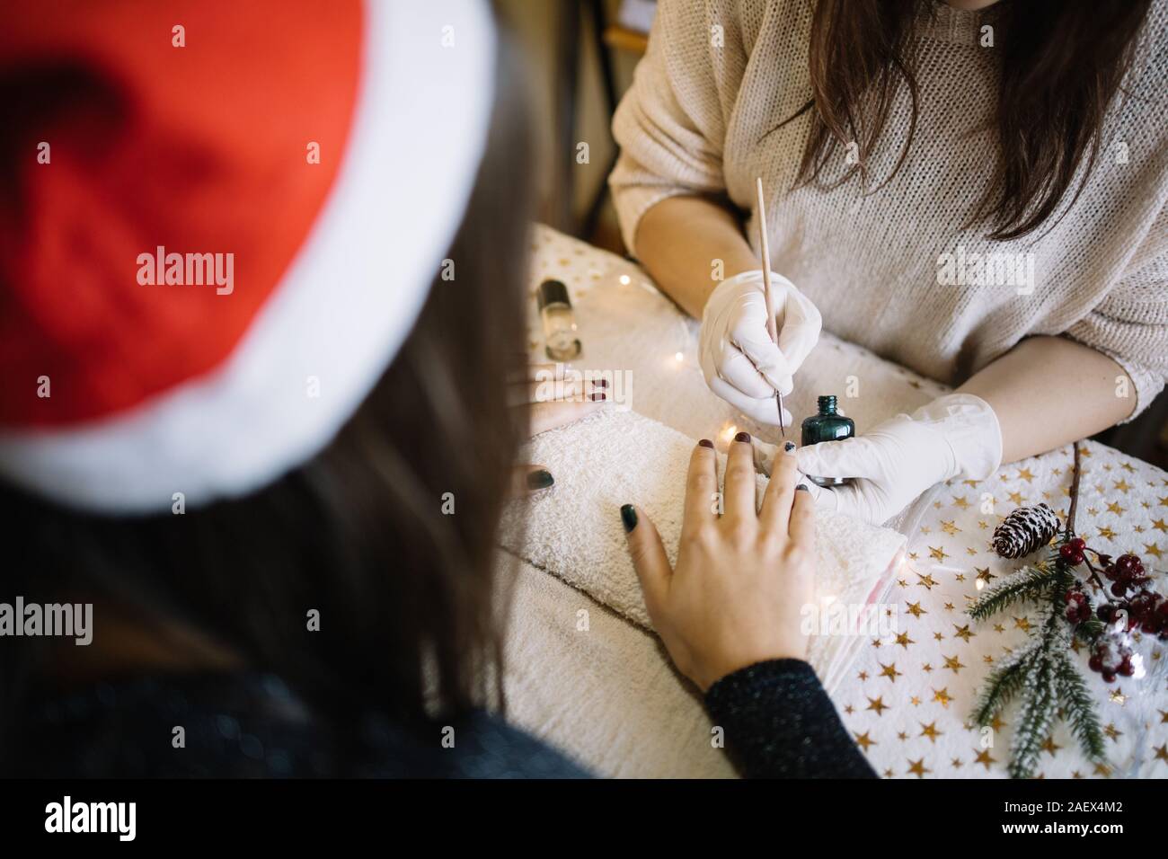 Weibliche Maniküre mit Pinsel malen auf Fingernägeln. Frau mit Weihnachtsmütze Erhalten ihr der Nägel aus kosmetikerin im Schönheitssalon mit Weihnachten getan d Stockfoto