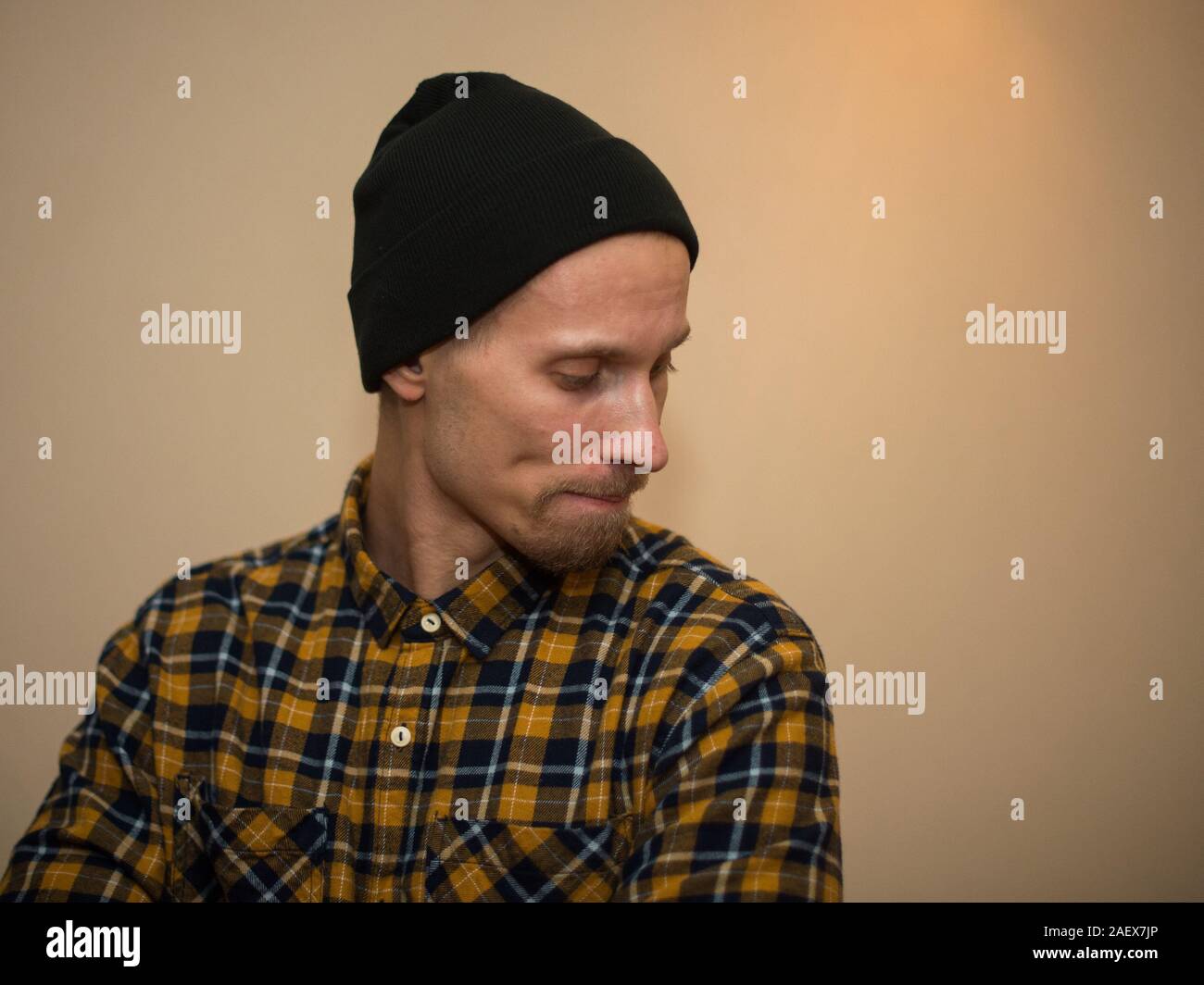 Junger Mann, Modell der Mode, trug einen karierten Hemd mit einem biege blind hinter ihm. Kerl in schwarzer Hut mit Bart im lässigen Stil. Stockfoto