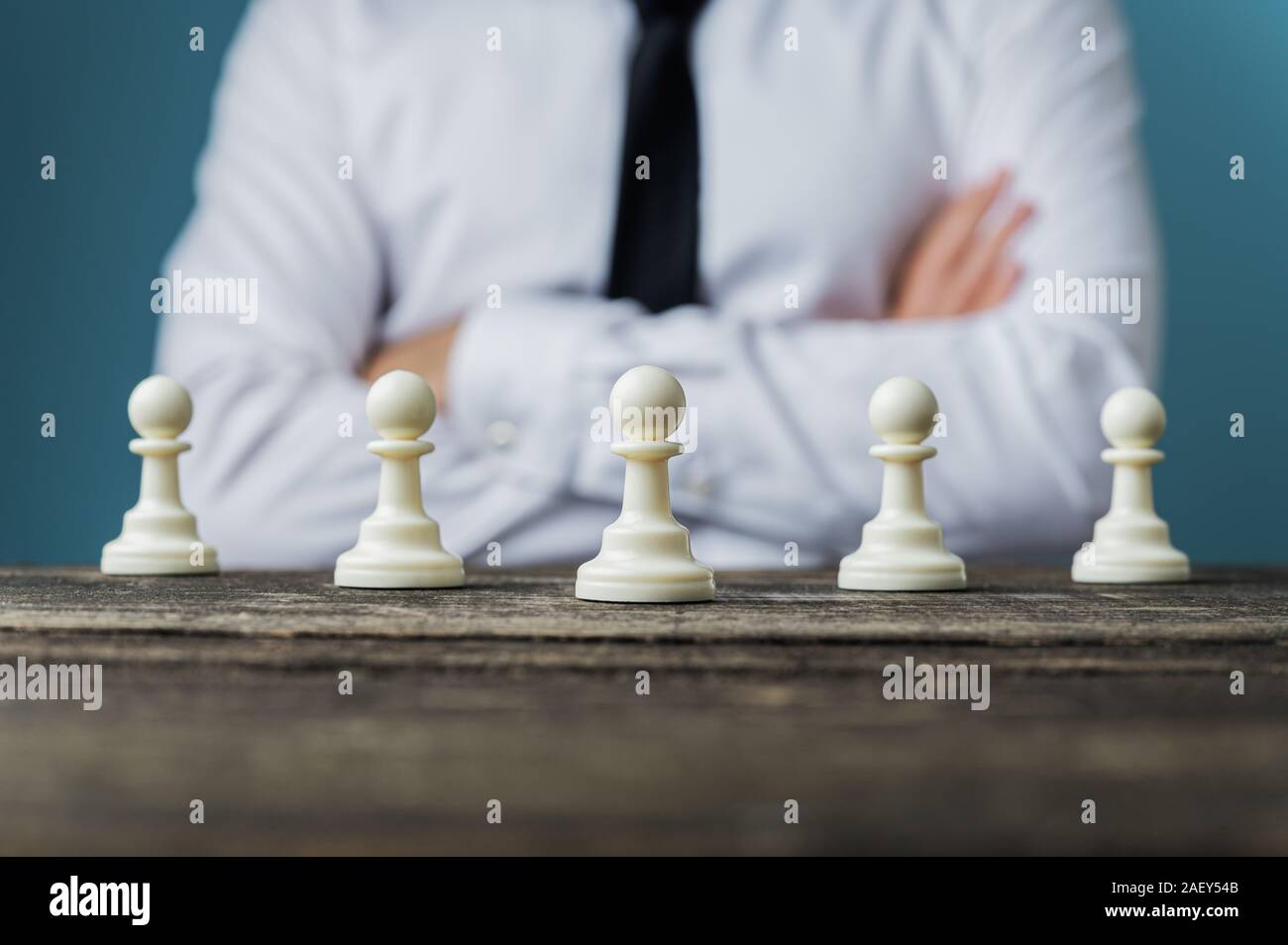 Geschäftsmann mit verschränkten Armen sitzt hinter einem Schreibtisch mit Schach schachfigur Stücke auf es in einem konzeptionellen Bild platziert. Stockfoto