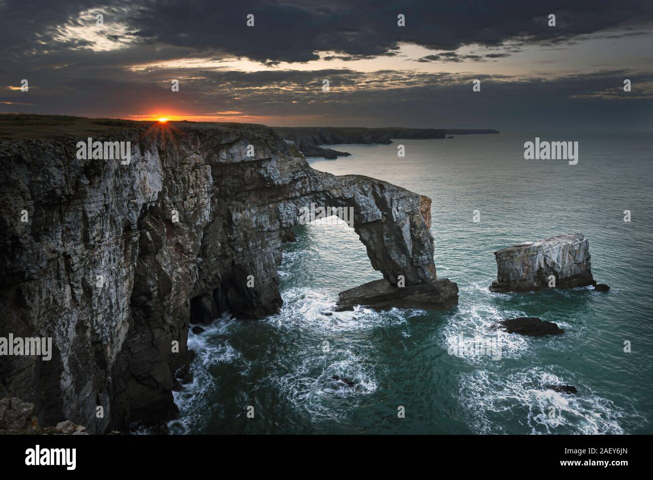 Sonnenaufgang mit Moody Himmel über Grüne Brücke von Wales, berühmten, natürlichen Felsbogen, beliebte Sehenswürdigkeit, Touristen Attraktion auf dramatische Küste von Pembrokeshire. Stockfoto