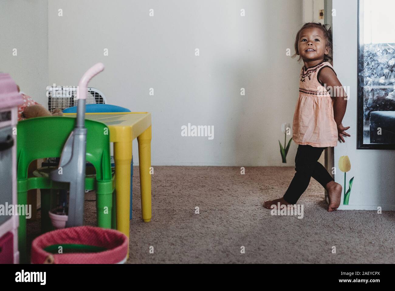 Lächelnd 2 Jahre alten multirassischen stehendes Mädchen barfuß auf dem Teppich von Wand Stockfoto