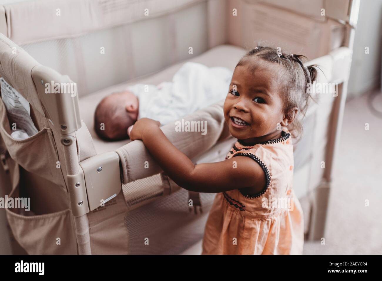 Lächelnd Multirassischen 2 Jahre alten Holding Krippe der schlafenden Baby Schwester Stockfoto